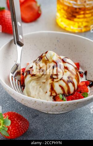 Fromage burrata gastronomique avec tartare de fraise à la menthe, au miel et au balsamique dans une assiette légère sur fond de béton gris ou de pierre. Petit déjeuner. Délique Banque D'Images