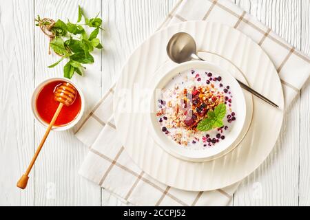 Avoine granola aux framboises séchées, bleuets et noix au lait et recouverte de miel dans un bol blanc sur une table en bois, vue sur le paysage depuis le dessus, Banque D'Images