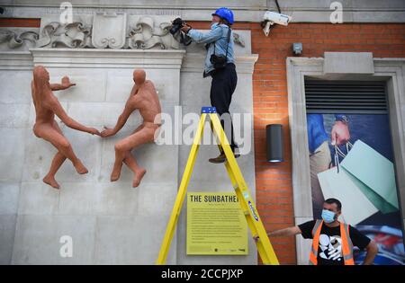 Un photographe prend une photo des baigneurs de soleil, une sculpture de l'artiste hongrois Peter Laszlo Peri retourne à Londres Waterloo après une absence de près de 70 ans. La sculpture, initialement exposée à l'entrée de la station de métro accueillant les visiteurs du Festival de Grande-Bretagne en 1951, a été considérée comme perdue, mais elle a été redécouverte dans le domaine d'un hôtel du sud-est de Londres cassé et peint un rose pâle. Une campagne de financement participatif a permis de recueillir des fonds pour que les couches de peinture soient retirées afin de les restaurer à la couleur terre cuite d'origine embrassée par le soleil. Banque D'Images