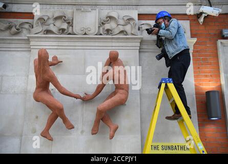 Un photographe prend une photo des baigneurs de soleil, une sculpture de l'artiste hongrois Peter Laszlo Peri retourne à Londres Waterloo après une absence de près de 70 ans. La sculpture, initialement exposée à l'entrée de la station de métro accueillant les visiteurs du Festival de Grande-Bretagne en 1951, a été considérée comme perdue, mais elle a été redécouverte dans le domaine d'un hôtel du sud-est de Londres cassé et peint un rose pâle. Une campagne de financement participatif a permis de recueillir des fonds pour que les couches de peinture soient retirées afin de les restaurer à la couleur terre cuite d'origine embrassée par le soleil. Banque D'Images