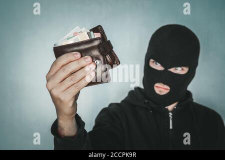 Un jeune homme mal intenté portant un masque noir tient le sac à main des hommes en cuir noir et regarde son butin. Le voleur a volé le portefeuille. Demi-coup de voleur dedans Banque D'Images