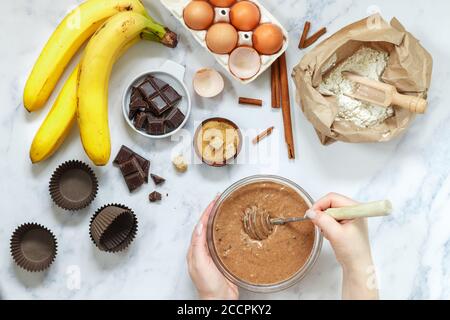 Femme prépare de la pâte pour des muffins faits maison avec de la banane et du chocolat. Fouetter pour fouetter dans les mains. Ingrédients sur la table - farine de blé, oeufs, bruns Banque D'Images