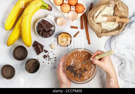 Femme prépare de la pâte pour des muffins faits maison avec de la banane et du chocolat. Fouetter pour fouetter dans les mains. Ingrédients sur la table - farine de blé, oeufs, bruns Banque D'Images