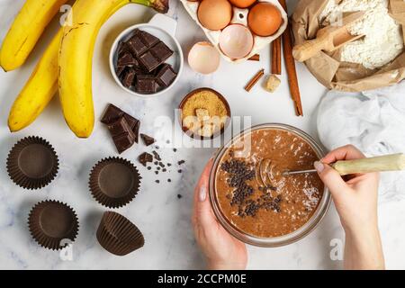 Femme prépare de la pâte pour des muffins faits maison avec de la banane et du chocolat. Fouetter pour fouetter dans les mains. Ingrédients sur la table - farine de blé, oeufs, bruns Banque D'Images