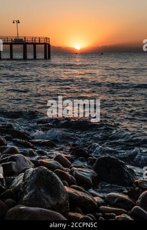 Lever du soleil depuis une plage de galets avec une passerelle vers le mer Banque D'Images