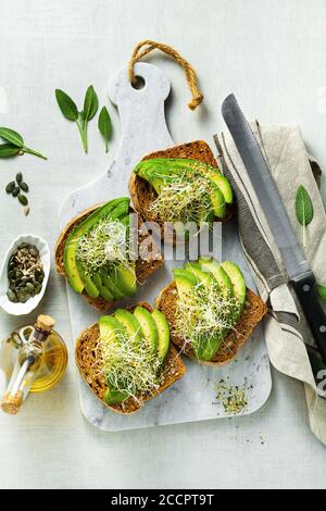 des sandwiches maison au pain de tomate avec des graines et des tomates séchées, servis avec de l'avocat, des pousses et des graines de chanvre. un petit-déjeuner ou une collation sains le matin Banque D'Images