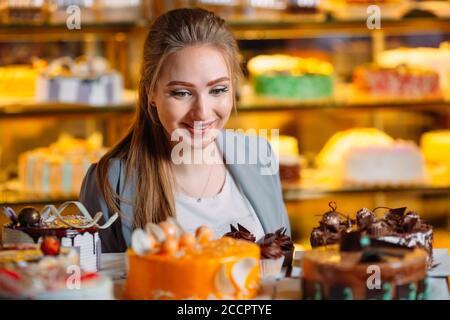 Fille regardant la fenêtre de la boulangerie avec différents morceaux de gâteaux. Banque D'Images