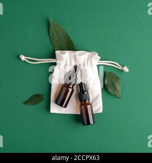 Des produits bio-cosmétiques écologiques sont mis en place sur fond vert. Produits de beauté zéro déchet - flacons compte-gouttes en verre ambré de sérum et sac en coton avec plante verte lea Banque D'Images
