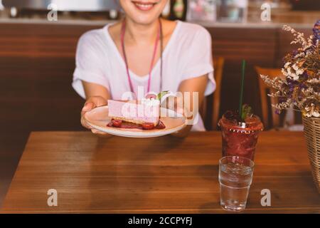 Femme tenant une assiette de tranche de gâteau de mousse de cassis dans le café. Banque D'Images