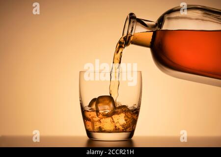 Un verre de whisky sur les rochers. Verser du Bourbon ou du cognac dans une bouteille de liqueur. Fond orange Banque D'Images