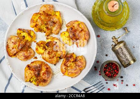 Pommes de terre entières écrasées et croustillantes cuites avec une croûte de sel de mer, d'huile d'olive, d'ail, de poivre et de thym dans une assiette blanche sur fond de béton gris. Rôti Banque D'Images