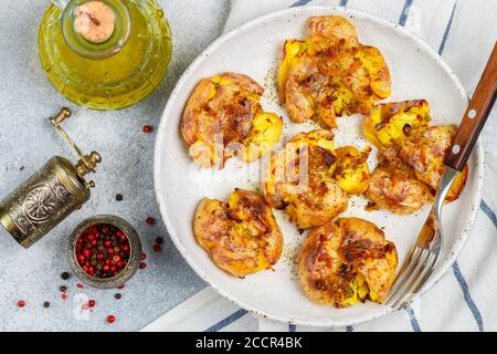 Pommes de terre entières écrasées et croustillantes cuites avec une croûte de sel de mer, d'huile d'olive, d'ail, de poivre et de thym dans une assiette blanche sur fond de béton gris. Rôti Banque D'Images