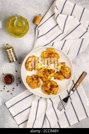 Pommes de terre entières écrasées et croustillantes cuites avec une croûte de sel de mer, d'huile d'olive, d'ail, de poivre et de thym dans une assiette blanche sur fond de béton gris. Rôti Banque D'Images