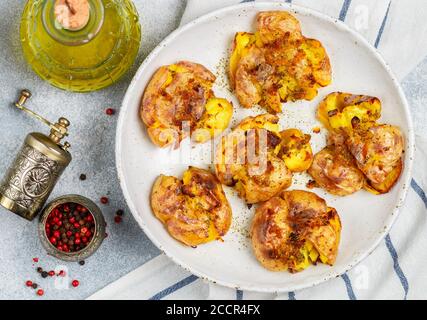 Pommes de terre entières écrasées et croustillantes cuites avec une croûte de sel de mer, d'huile d'olive, d'ail, de poivre et de thym dans une assiette blanche sur fond de béton gris. Rôti Banque D'Images