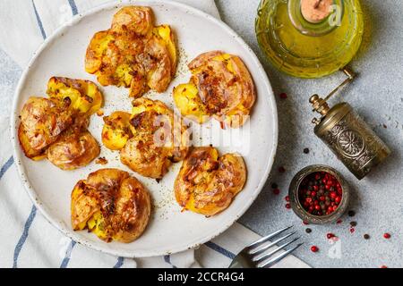 Pommes de terre entières écrasées et croustillantes cuites avec une croûte de sel de mer, d'huile d'olive, d'ail, de poivre et de thym dans une assiette blanche sur fond de béton gris. Rôti Banque D'Images