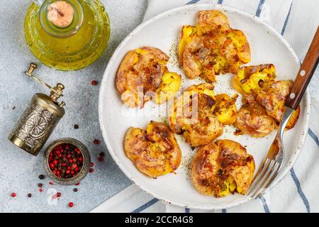 Pommes de terre entières écrasées et croustillantes cuites avec une croûte de sel de mer, d'huile d'olive, d'ail, de poivre et de thym dans une assiette blanche sur fond de béton gris. Rôti Banque D'Images