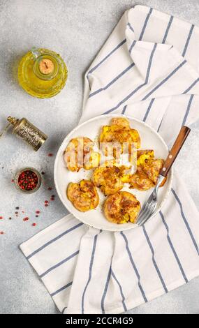 Pommes de terre entières écrasées et croustillantes cuites avec une croûte de sel de mer, d'huile d'olive, d'ail, de poivre et de thym dans une assiette blanche sur fond de béton gris. Rôti Banque D'Images