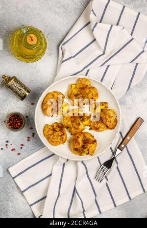 Pommes de terre entières écrasées et croustillantes cuites avec une croûte de sel de mer, d'huile d'olive, d'ail, de poivre et de thym dans une assiette blanche sur fond de béton gris. Rôti Banque D'Images