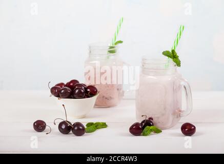 Cerises douces et smoothies au lait dans deux bocaux en verre avec une paille et des cerises douces dans une tasse, les cerises douces sont dispersées sur la table sur un béton Banque D'Images