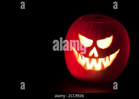 Jack O'Lantern illuminé effrayant halloween citrouille sculptée sur fond noir avec espace de copie. Banque D'Images