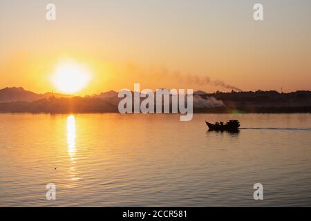 Magnifique coucher de soleil sur la rivière. Silhouette d'un bateau de pêche allant vers le soleil. Brouillard mystérieux et fumée à l'horizon. Espace d'édition. HPa-an, Myanmar Banque D'Images