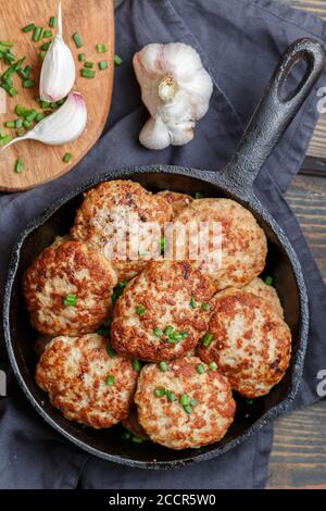 Délicieux poulet juteux ou côtelettes de dinde avec ail et oignons verts dans une casserole en fonte sur une table en bois sombre. Style rustique. Mise au point sélective, haut v Banque D'Images