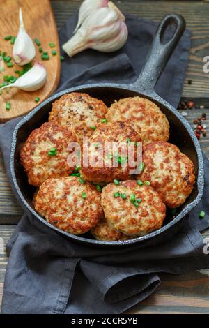 Délicieux poulet juteux ou côtelettes de dinde avec ail et oignons verts dans une casserole en fonte sur une table en bois sombre. Style rustique. Mise au point sélective, haut v Banque D'Images