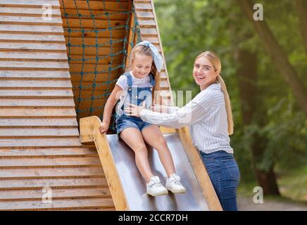 Mère Riding Kid Girl sur le toboggan sur le terrain de jeu à l'extérieur Banque D'Images