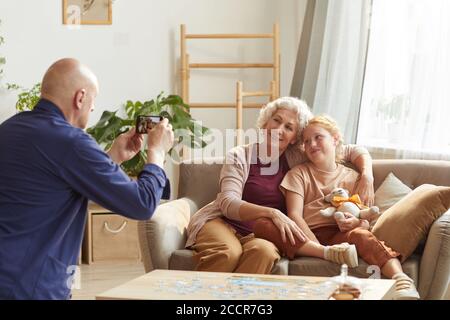 Portrait ton chaud d'un homme âgé prenant une photo de femme et de petite-fille sur smartphone pour des souvenirs de famille, espace de copie Banque D'Images