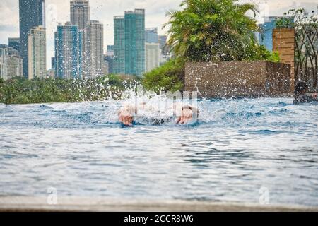 Manille, Philippines - 02 février 2020. Un homme nage un papillon dans une piscine sur le toit d'un hôtel de luxe. Vue sur la ville de Manille depuis la piscine Banque D'Images