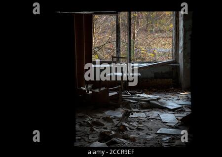 Salle de classe avec chaises cassées et carnets abandonnés dans une école abandonnée à Pripyat, zone d'exclusion de Tchernobyl, Ukraine Banque D'Images