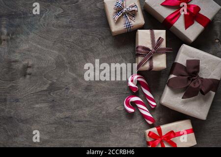 De nombreuses boîtes-cadeaux enveloppées dans du papier brun et liées avec différents rubans et bonbons de Noël se trouvent sur un fond en bois, vue de dessus, Copy space.Christma Banque D'Images