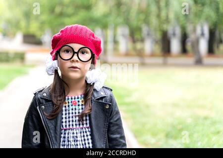 une petite fille drôle dans une casquette rouge et ronde les lunettes se loquent dans le cadre Banque D'Images