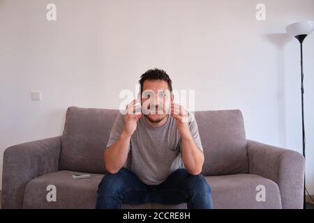 Portrait d'un jeune homme excité assis sur un canapé regardant son équipe sportive, qui est sur le point de marquer des points. Banque D'Images