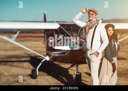 Jeune couple de mode rétro se posant devant un petit avion Banque D'Images