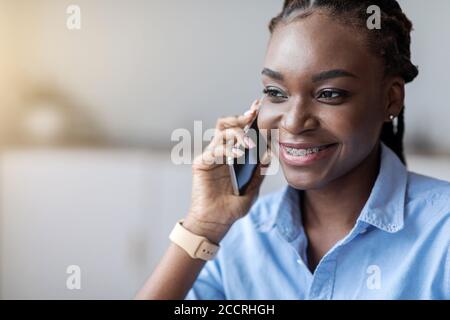 Appel téléphonique. Femme afro-américaine souriante avec bretelles parlant sur téléphone portable Banque D'Images