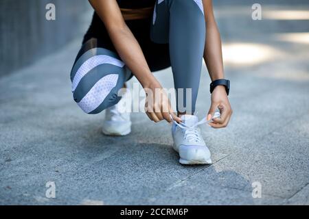 Gros plan de la fille noire dans les vêtements de sport nouant des lacets de chaussures avant le jogging Banque D'Images