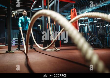 Homme de fitness s'entraîner avec des cordes de combat à la salle de gym. Banque D'Images