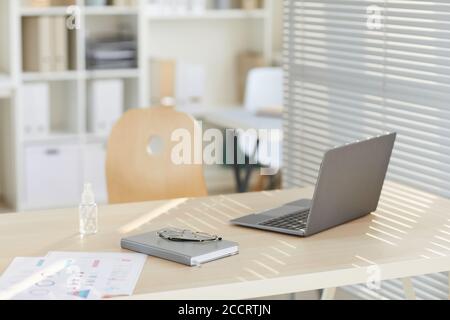 Image d'arrière-plan d'un bureau vide avec ordinateur portable et assainisseur pour les mains éclairé par la lumière du soleil dans un bureau moderne post-pandémie, espace de copie Banque D'Images