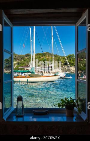 Vue sur les yachts sur l'eau claire comme vu à travers une fenêtre de café à Longos, Paxos, Iles Ioniennes, Grèce Banque D'Images