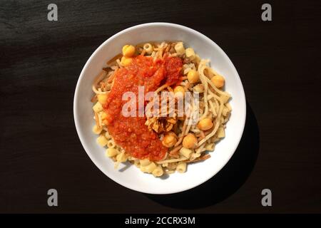 Célèbre arabe traditionnel, plat égyptien - Koshari. National Kushari dans une plaque blanche sur fond de bois foncé. Flat lay, vue de dessus. Banque D'Images