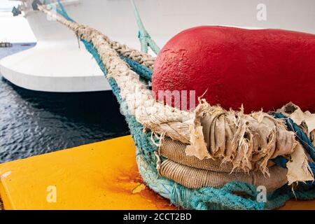 Corde marine épaisse et recouverte d'intempéries autour d'un bollard rouge, amarré un grand bateau de mer à un quai/quai jaune vif Banque D'Images