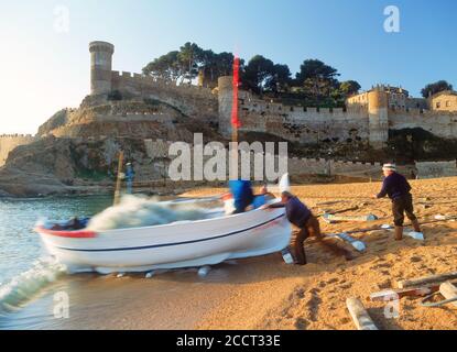 Pêcheurs poussant le bateau dans les vagues de la côte sur Tossa de Mar plage dans la province de Gérone en Espagne au lever du soleil Banque D'Images