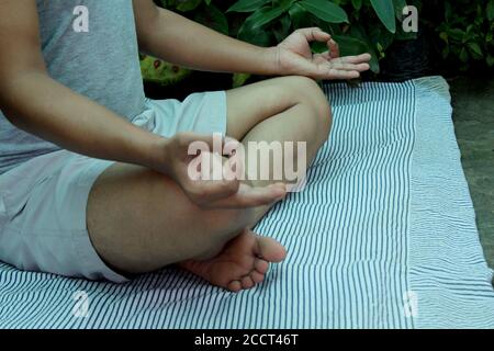 jeune homme pratiquant la méditation de yoga dans le parc vert, foyer sélectif avec flou. Banque D'Images