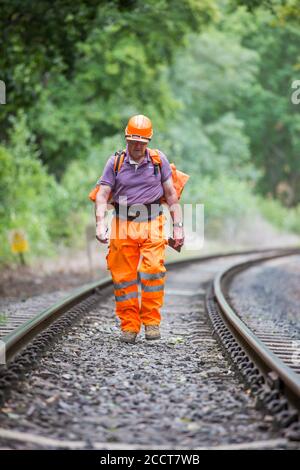 Travailleur ferroviaire, à l'avant, à pied isolé le long de la ligne de chemin de fer du patrimoine britannique, inspectant la voie pour les dommages. Entretien courant des chemins de fer, inspection. Banque D'Images