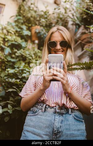 Bonne femme avec des lunettes de soleil regardant son smartphone dans le nature Banque D'Images