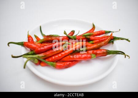 Les piments verts frais sont transformés en piments rouges mûrs avec tige verte. Les produits frais crus non séchés sont placés dans une plaque blanche avec un fond blanc. Chaud Indien asi Banque D'Images