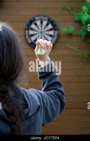 Une fille méconnaissable avec son dos à nous avec la flèche de fléchettes dans sa main vise un tableau cible de fléchettes. Concept de la cible et de l'objectif Banque D'Images