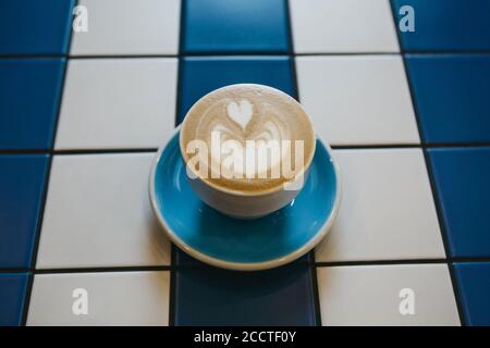 Gros plan de café cappuccino frais et aromatique dans une tasse bleue sur une table de carreaux de céramique bleu et blanc. Banque D'Images