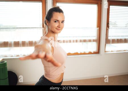 Portrait d'une belle femme en tenue sportive faisant du yoga avec bras étirés à la maison Banque D'Images